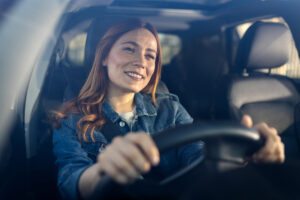 Smiling woman driving car, wearing seatbelt.