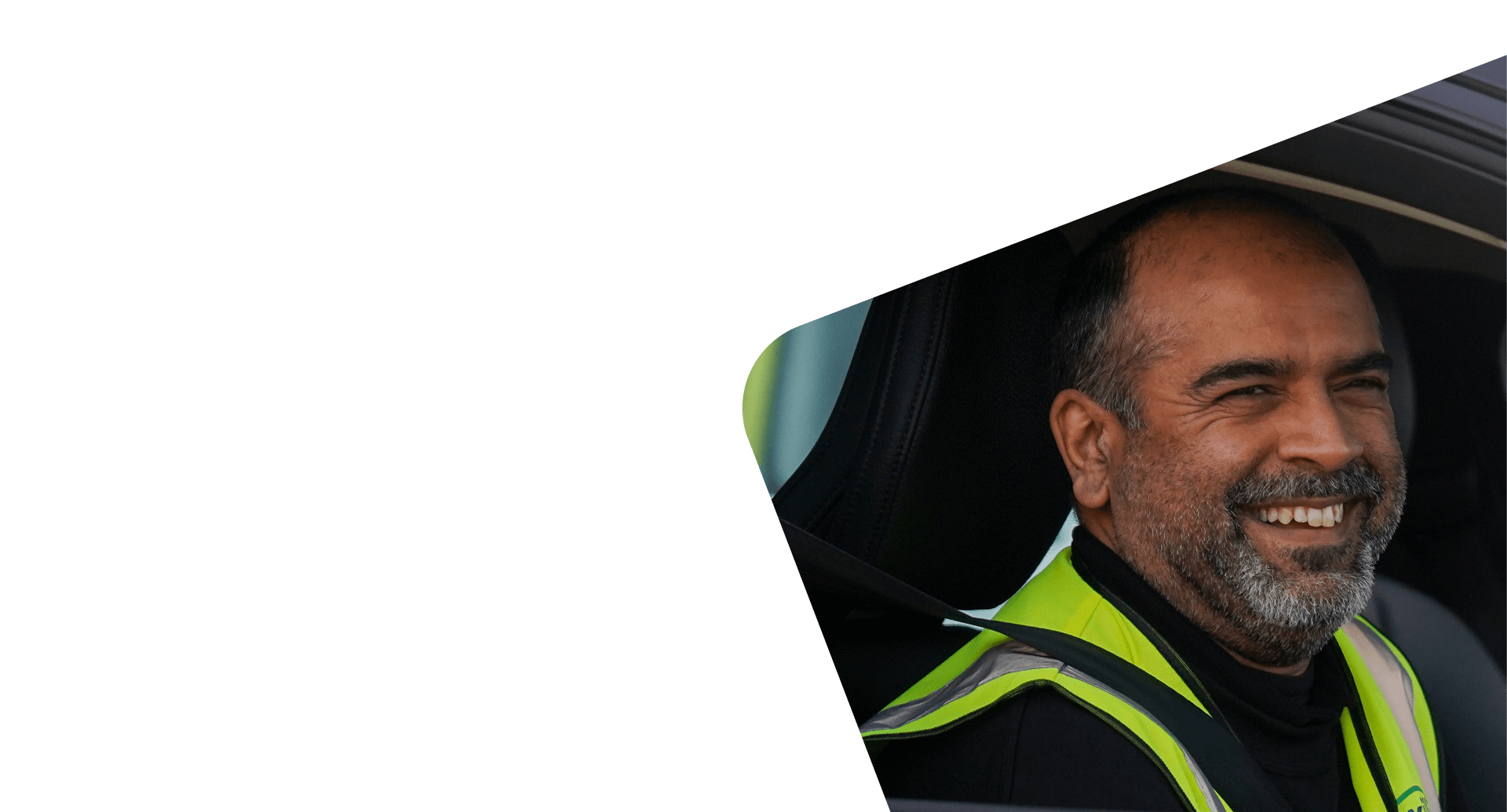 Smiling man in a car, wearing a lime-green safety vest.